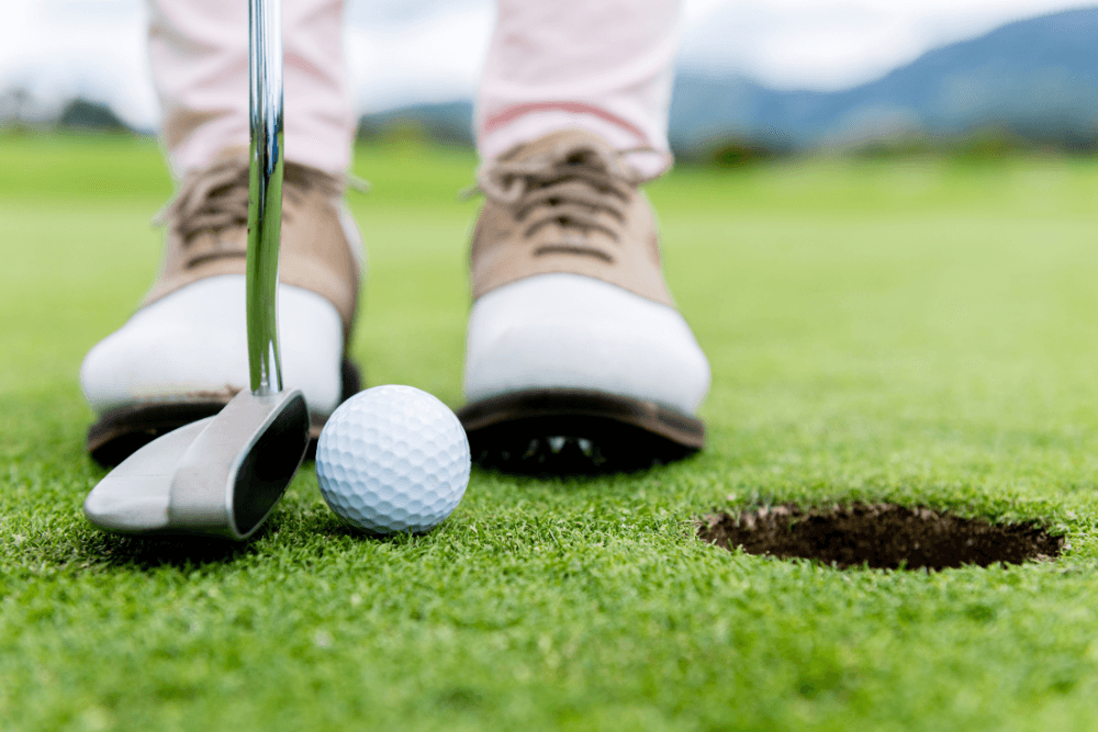 Close up of Man in golf shoes standing by hole with golf club