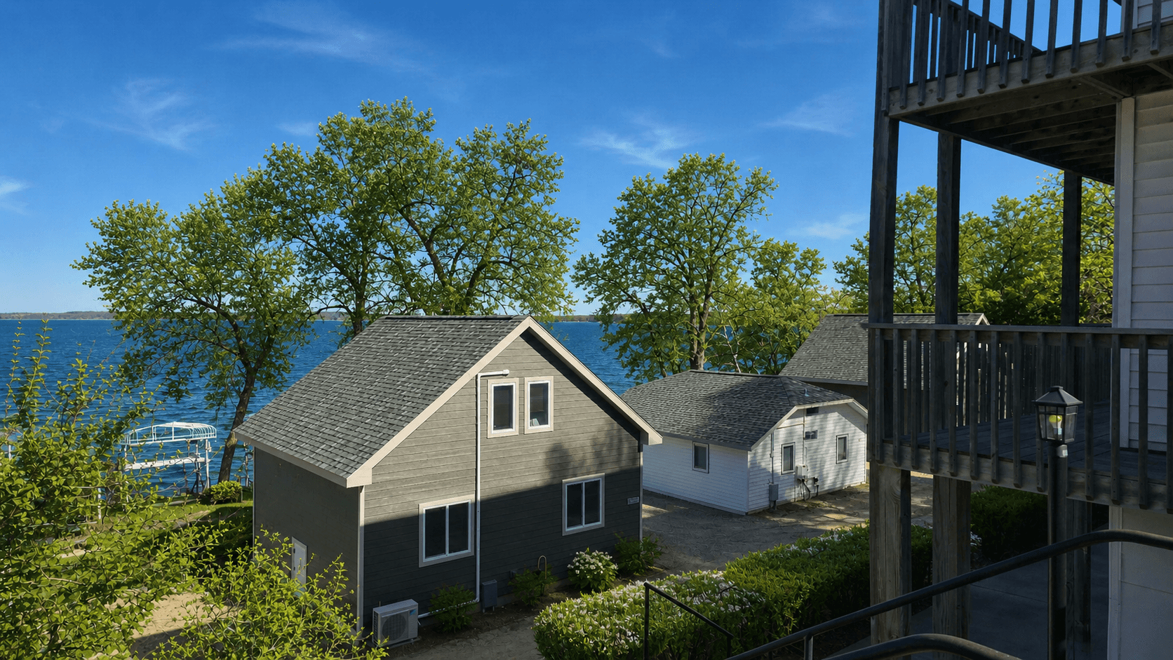 Scenic view of two houses surrounded by trees near a lake under a clear blue sky.