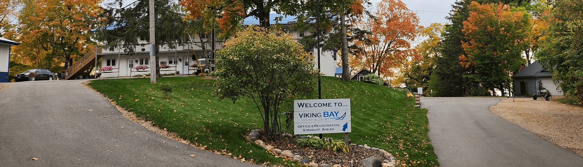 Curvy road with sign to Viking Bay Resort with fall colors, trees and grass with resort buildings in background