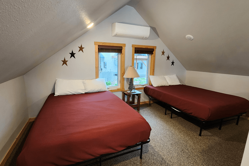 Two twin beds with red coverlets in vaulted attic type area with window on wall